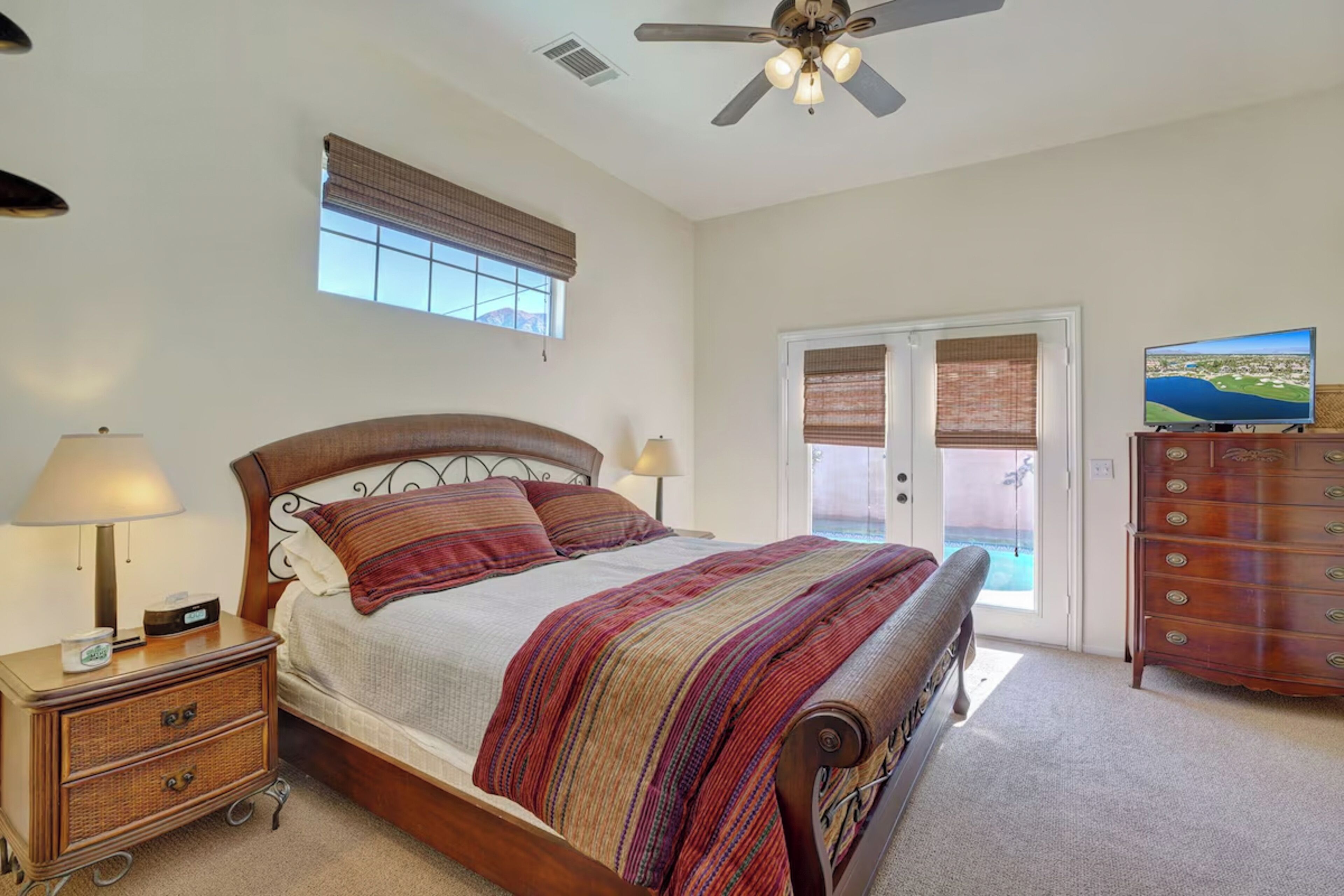 A bedroom with a bed, bedside tables, a dresser, a ceiling fan, and a window with blinds.