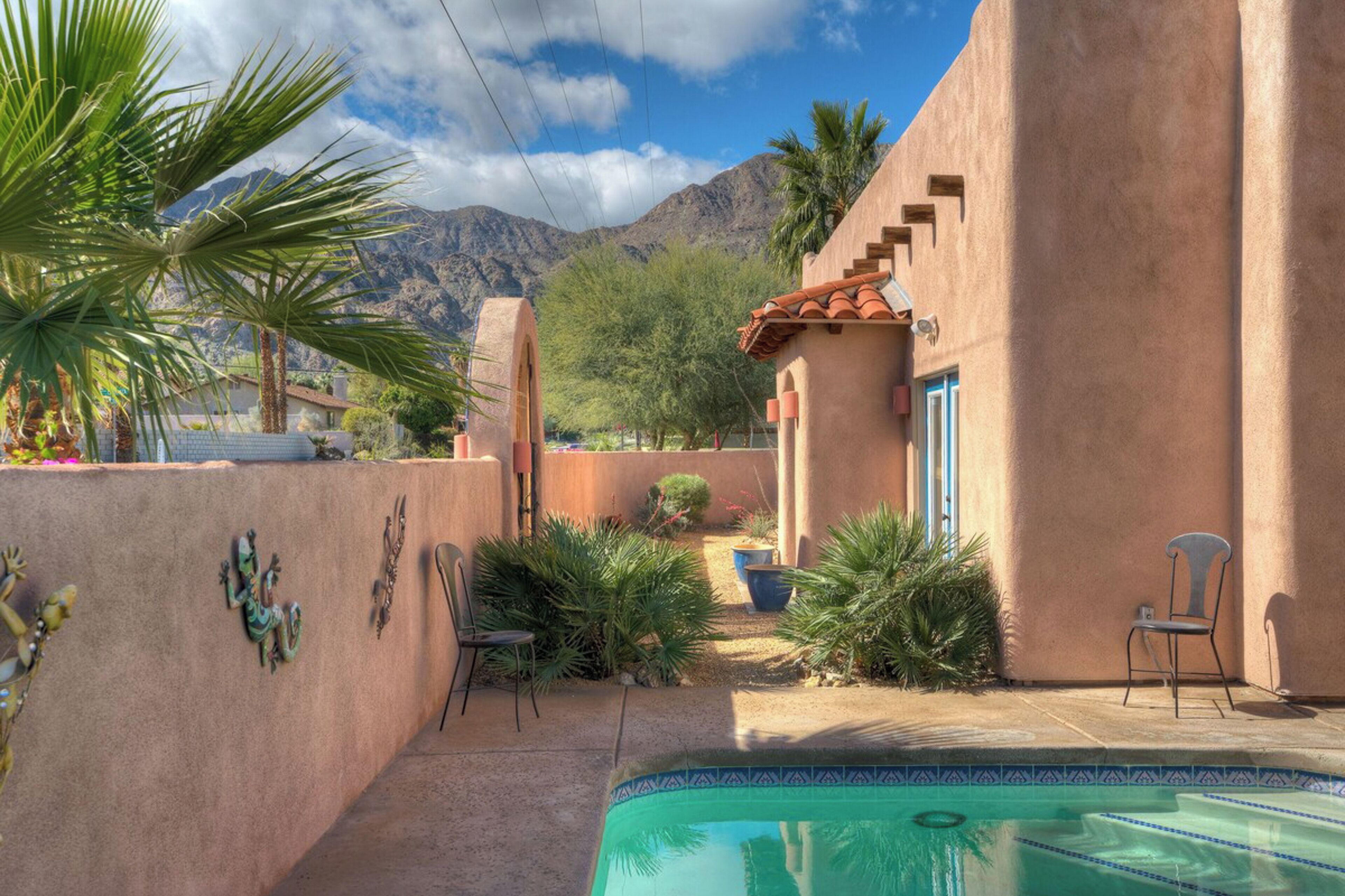 A pool area with a clear view of mountains, surrounded by a stucco building with a tiled roof and a blue door.