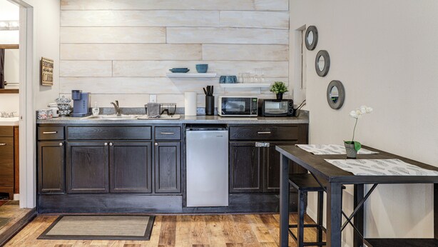 A modern kitchen with dark wood cabinets, a built-in dishwasher, a microwave, and a small table with a vase. - 9 Mi to Rangers & Cowboys Home Games: DFW Studio (Grand Prairie)
