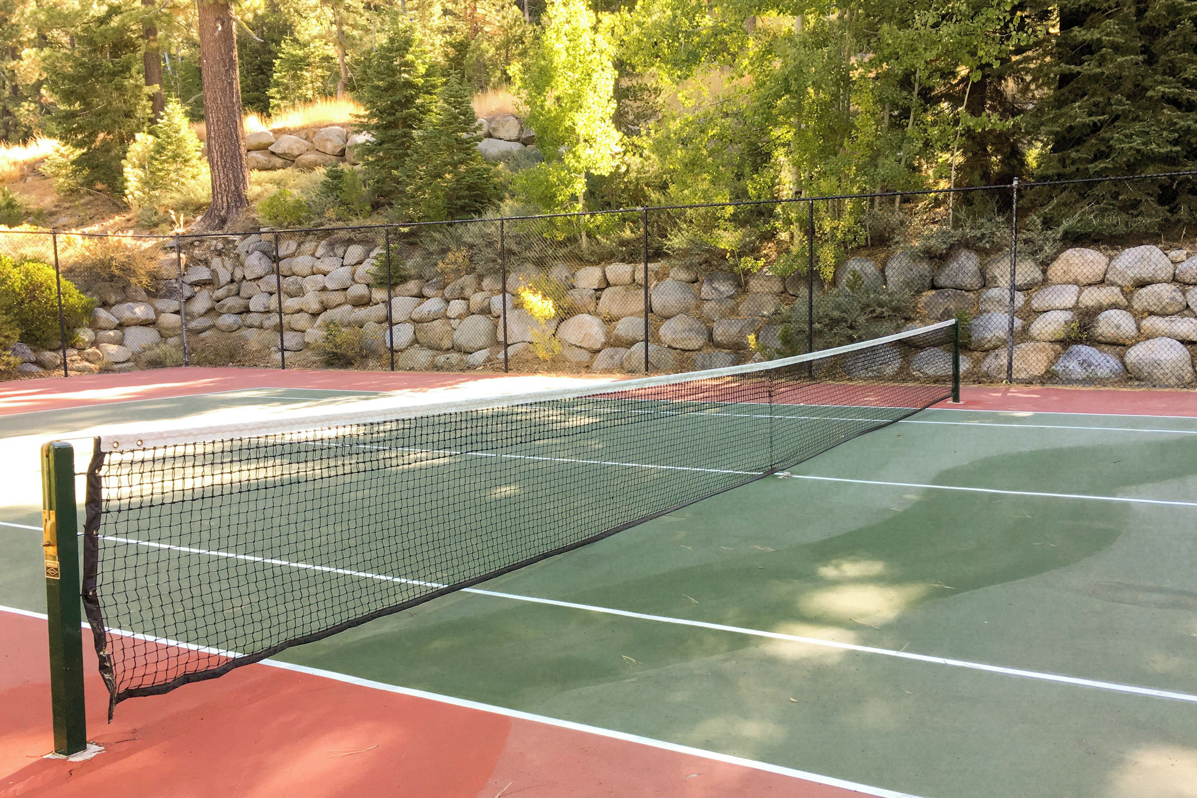 A tennis court with a net, surrounded by a stone wall and trees.