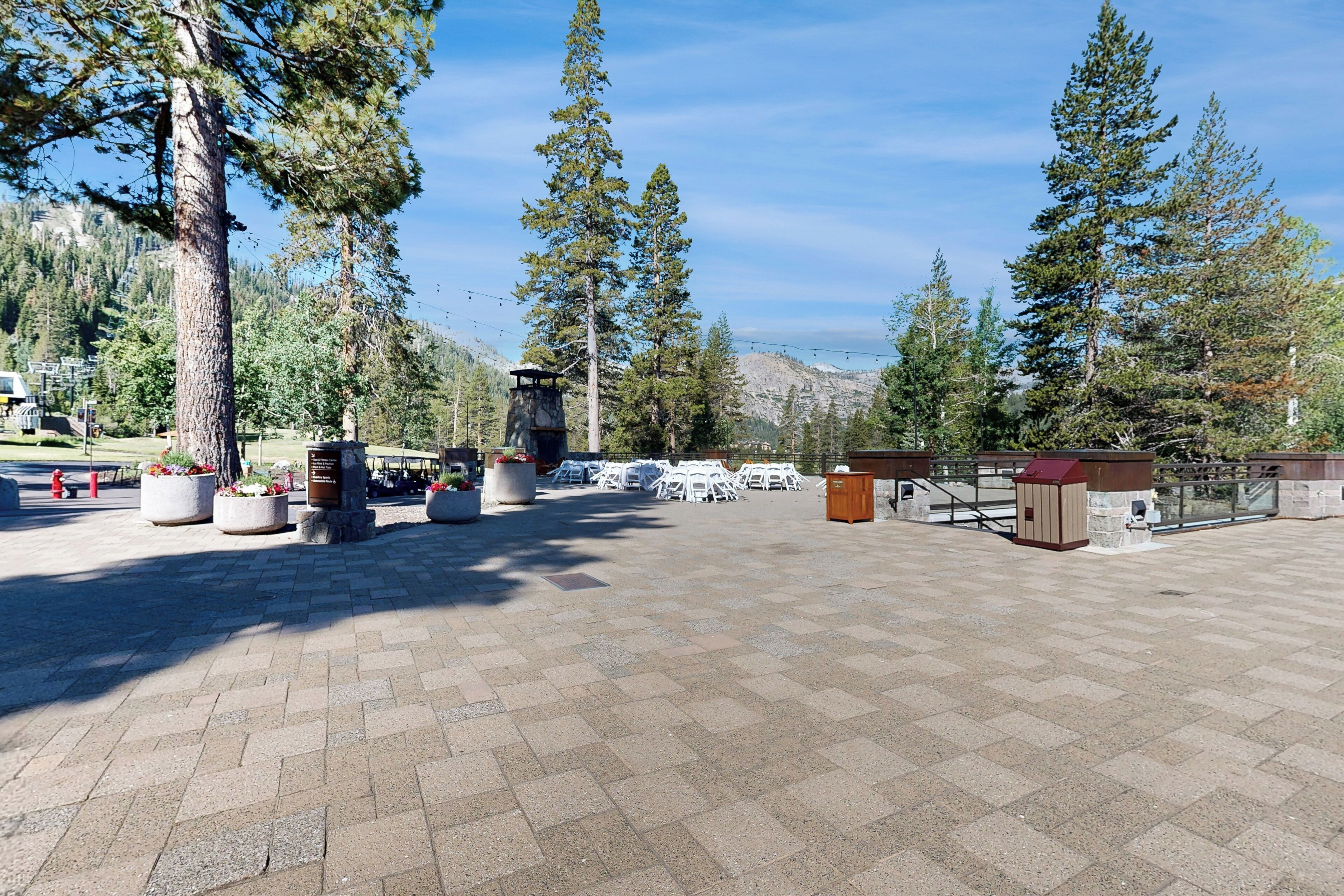 A paved outdoor area with seating arrangements, a stone monument, and a view of a mountainous landscape.