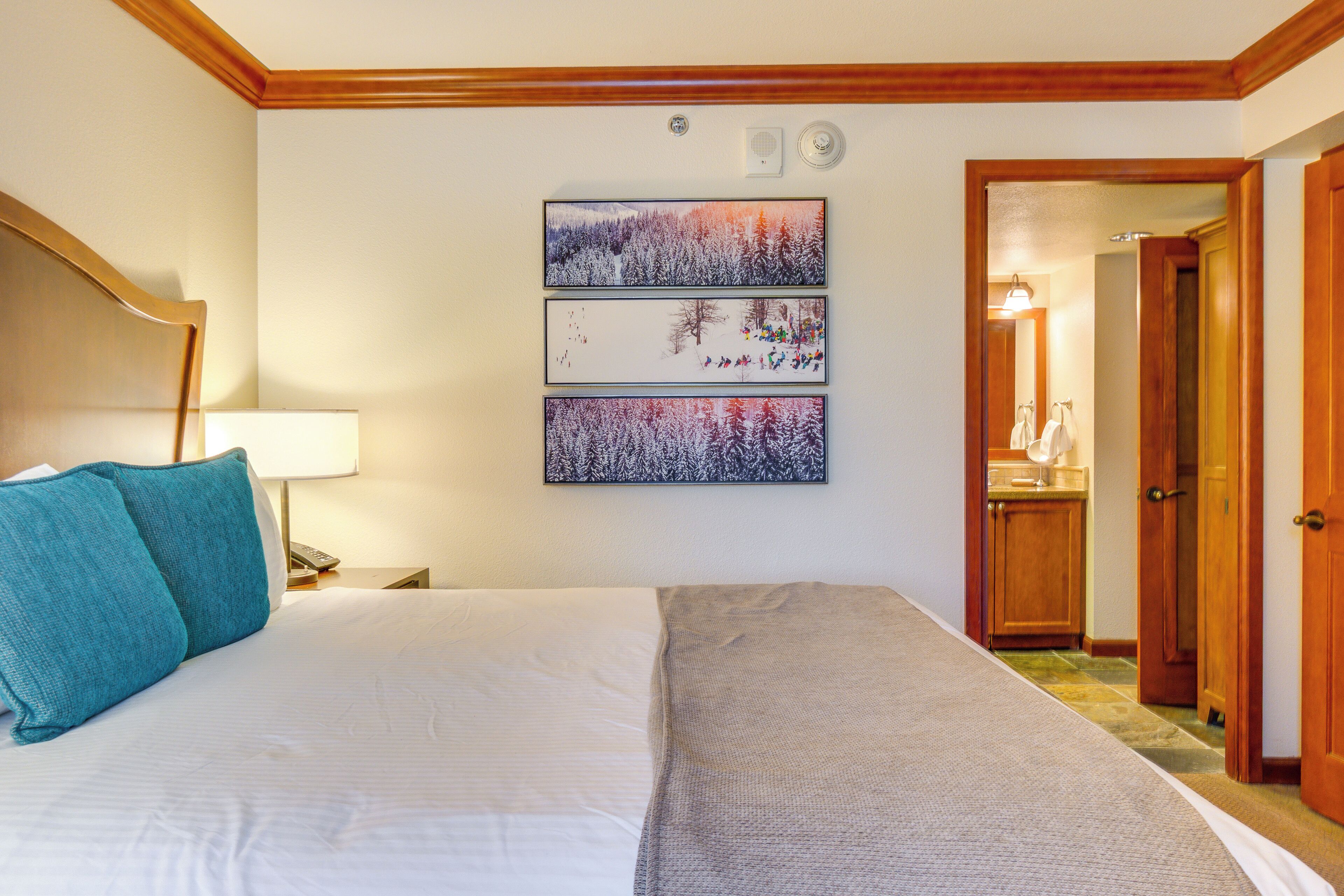 A hotel room with a large bed, a nightstand, a lamp, and a wall-mounted artwork depicting a snowy forest scene.