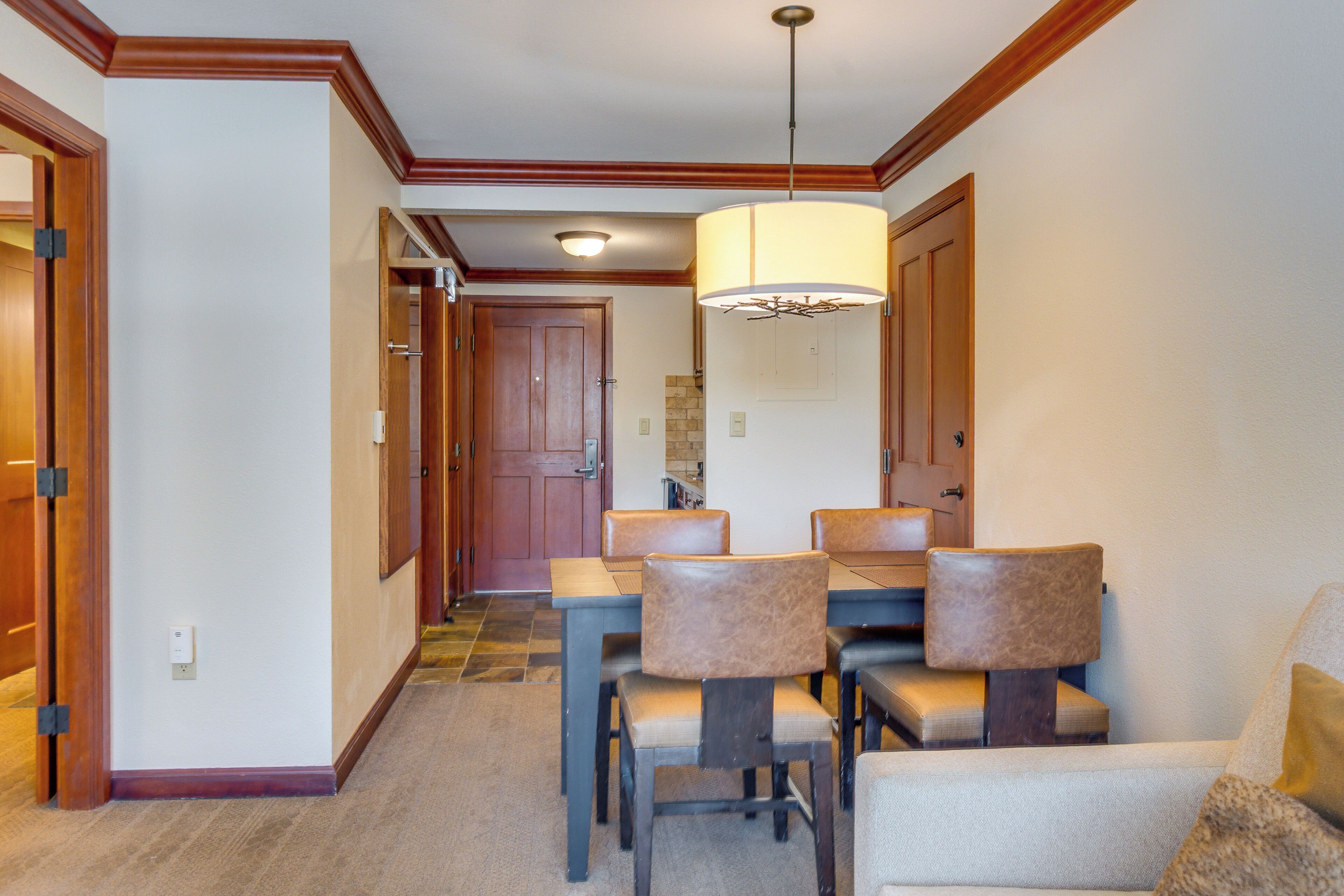 A dining area with a table and chairs, a hanging light fixture, and a wooden door in the background.