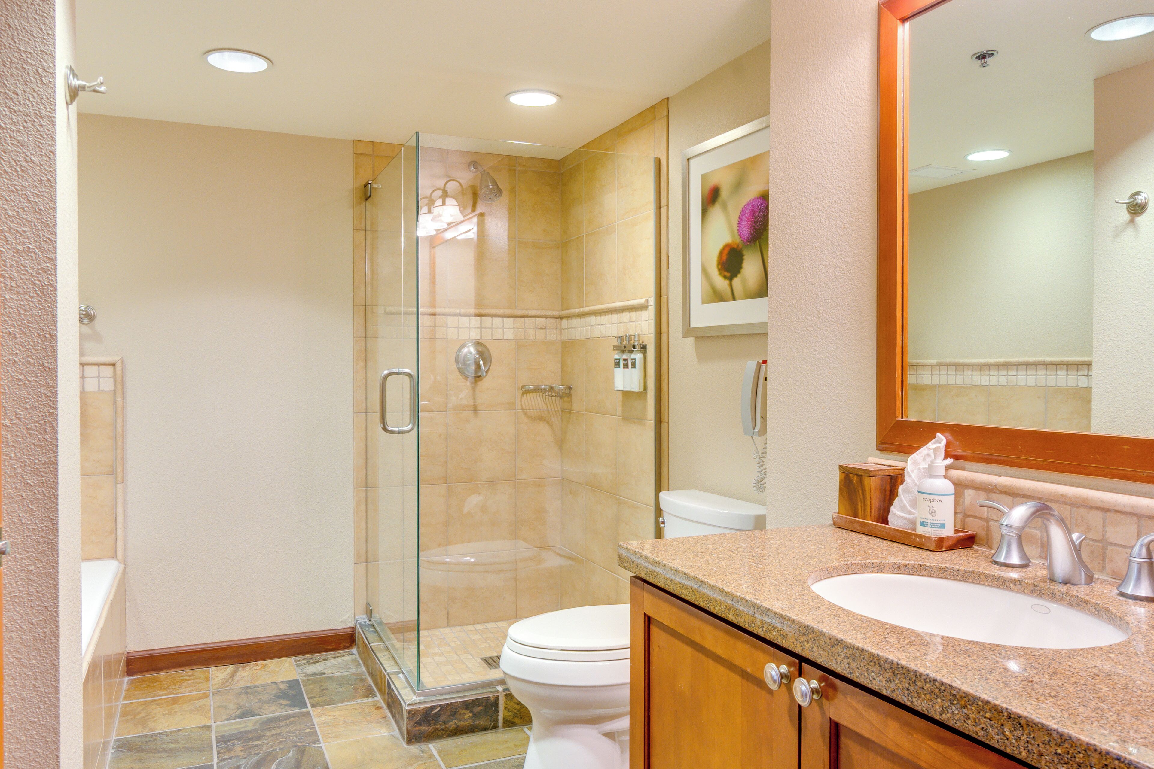 A modern bathroom with a glass-enclosed shower, a white toilet, and a granite countertop sink.