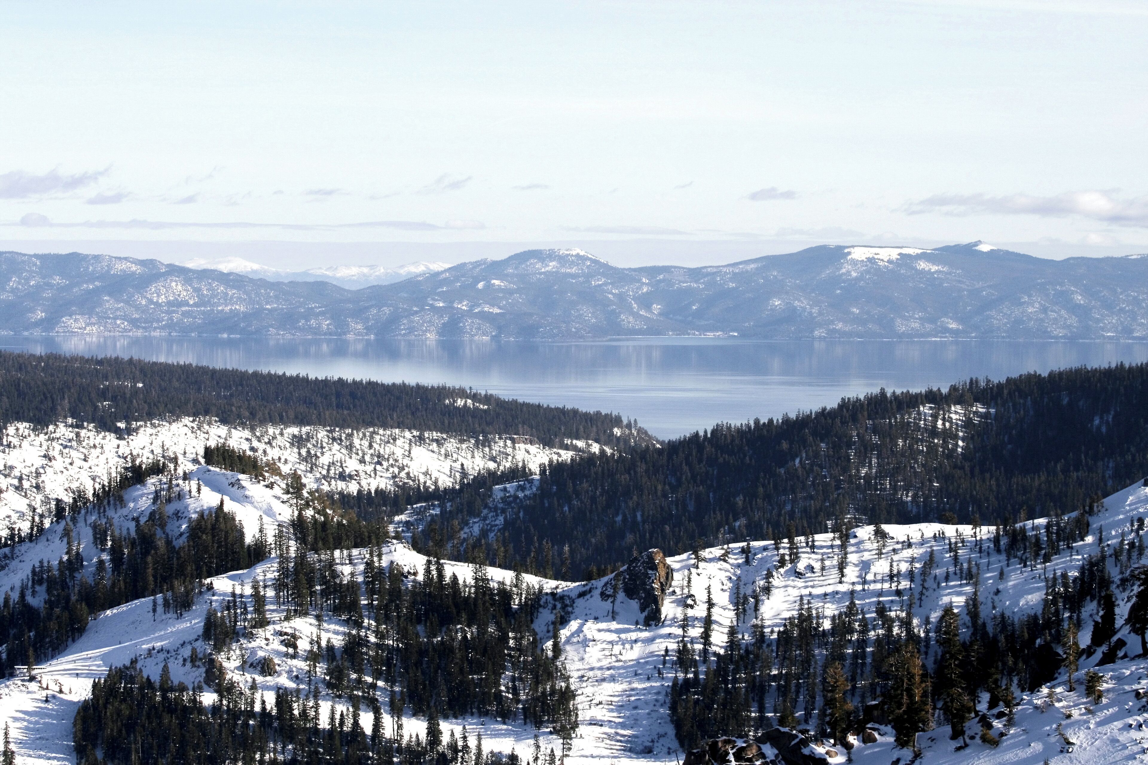 A panoramic view of a mountainous landscape with snow-covered slopes and a lake in the distance.