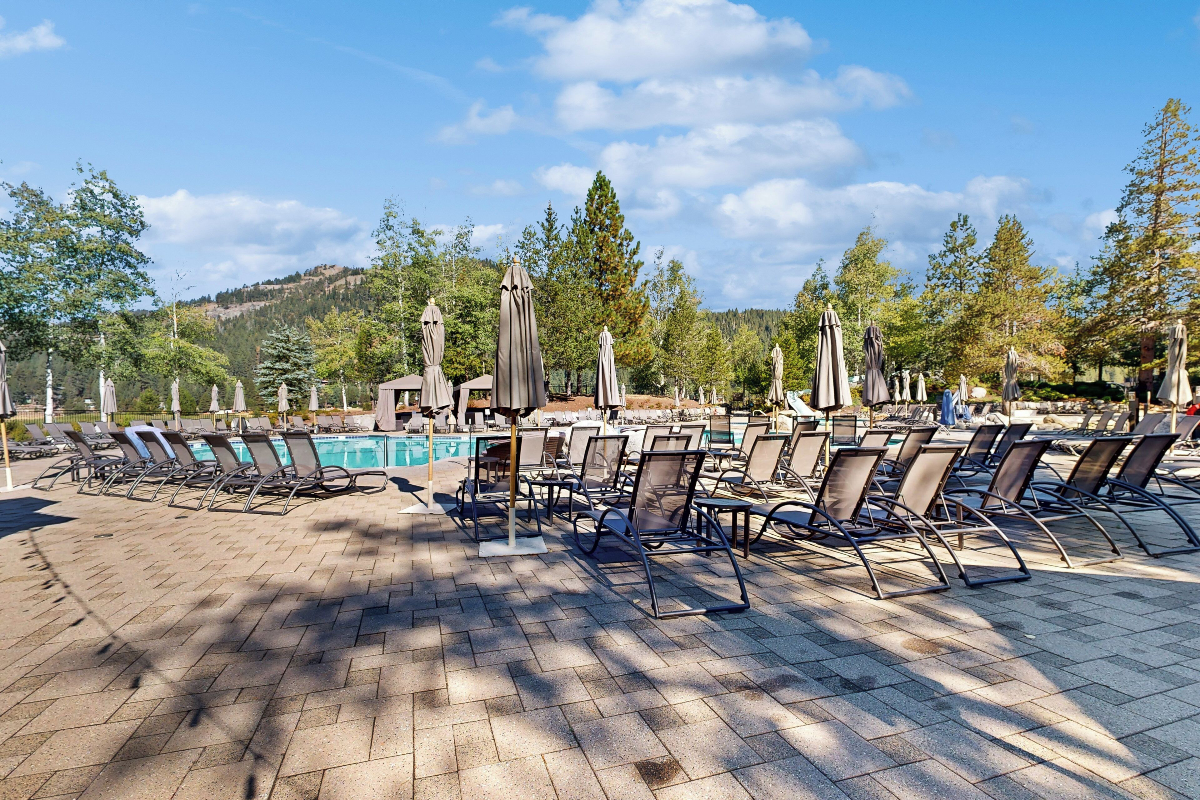 Zona de piscina con sillones de descanso y sombrillas, una piscina y un paisaje montañoso al fondo.
