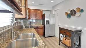 A modern kitchen with granite countertops, stainless steel appliances, wooden cabinets, and a decorative wall art piece. - Anna Maria Island Duplex: Pool, Kitchen, Sun Deck (Holmes Beach)