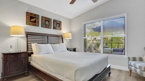 A bedroom with a large bed, two bedside lamps, a nightstand, a ceiling fan, and a window with blinds. - Anna Maria Island Duplex: Pool, Kitchen, Sun Deck (Holmes Beach)