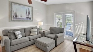 A living room with a grey sofa, ottoman, and a flat-screen TV on a glass table. - Anna Maria Island Duplex: Pool, Kitchen, Sun Deck (Holmes Beach)