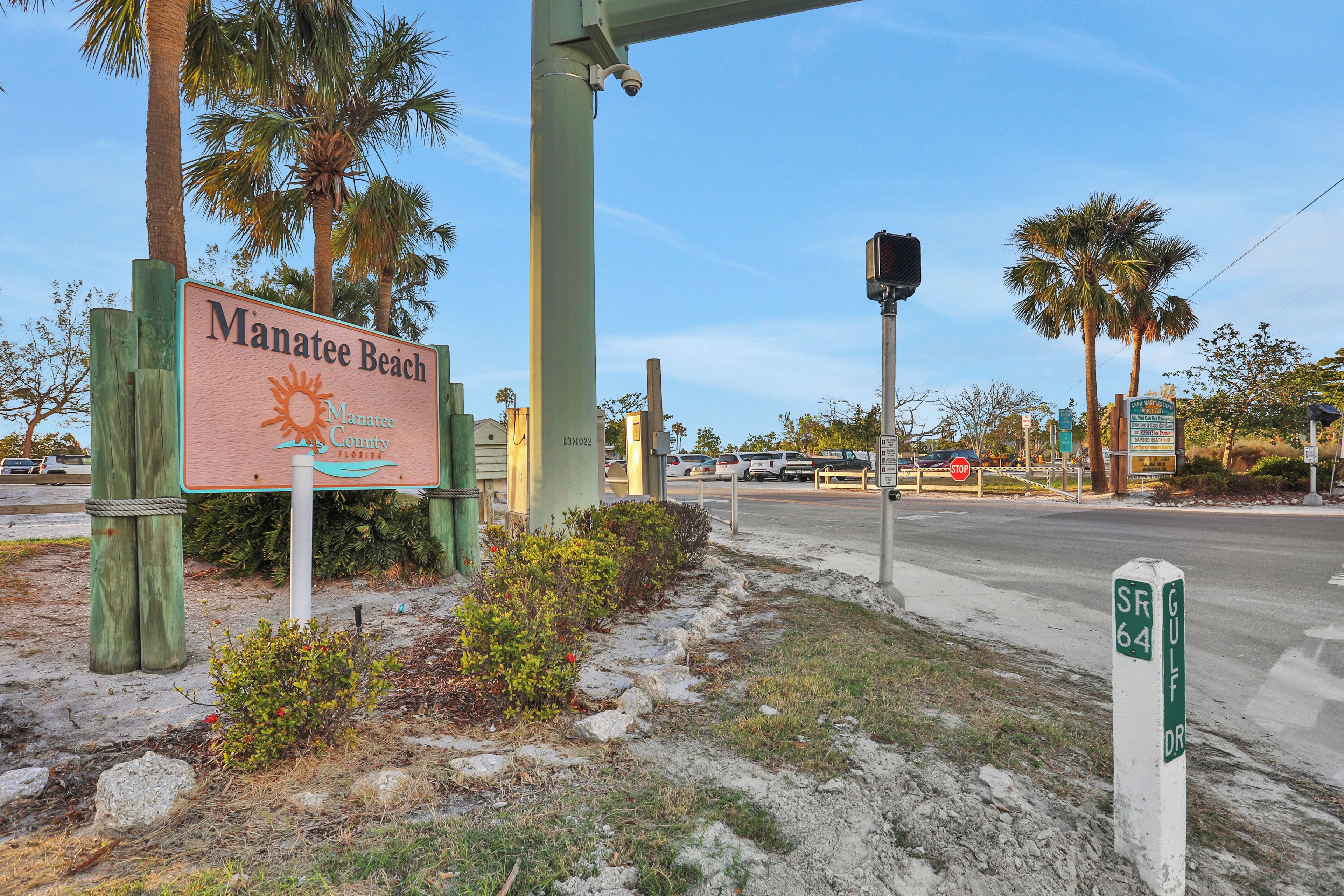 A sign for Manatee Beach in Manatee County, Florida, with a clear sky and palm trees in the background.