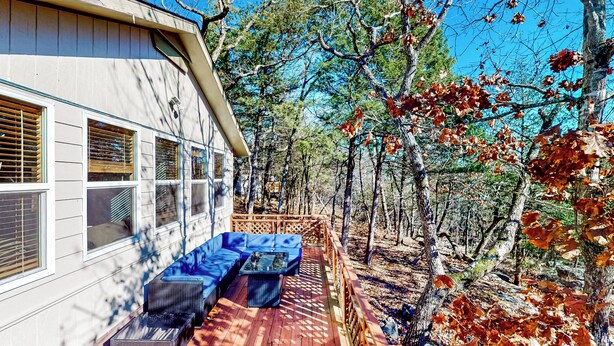 Une terrasse en bois avec des sièges d’extérieur, entourée d’arbres et d’une maison dotée de grandes fenêtres.