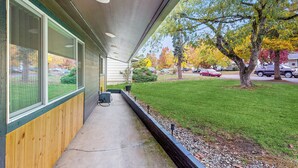 Un espace extérieur abrité, doté d’un chemin en béton, de bancs en bois et offrant une vue sur une pelouse verdoyante et des arbres.