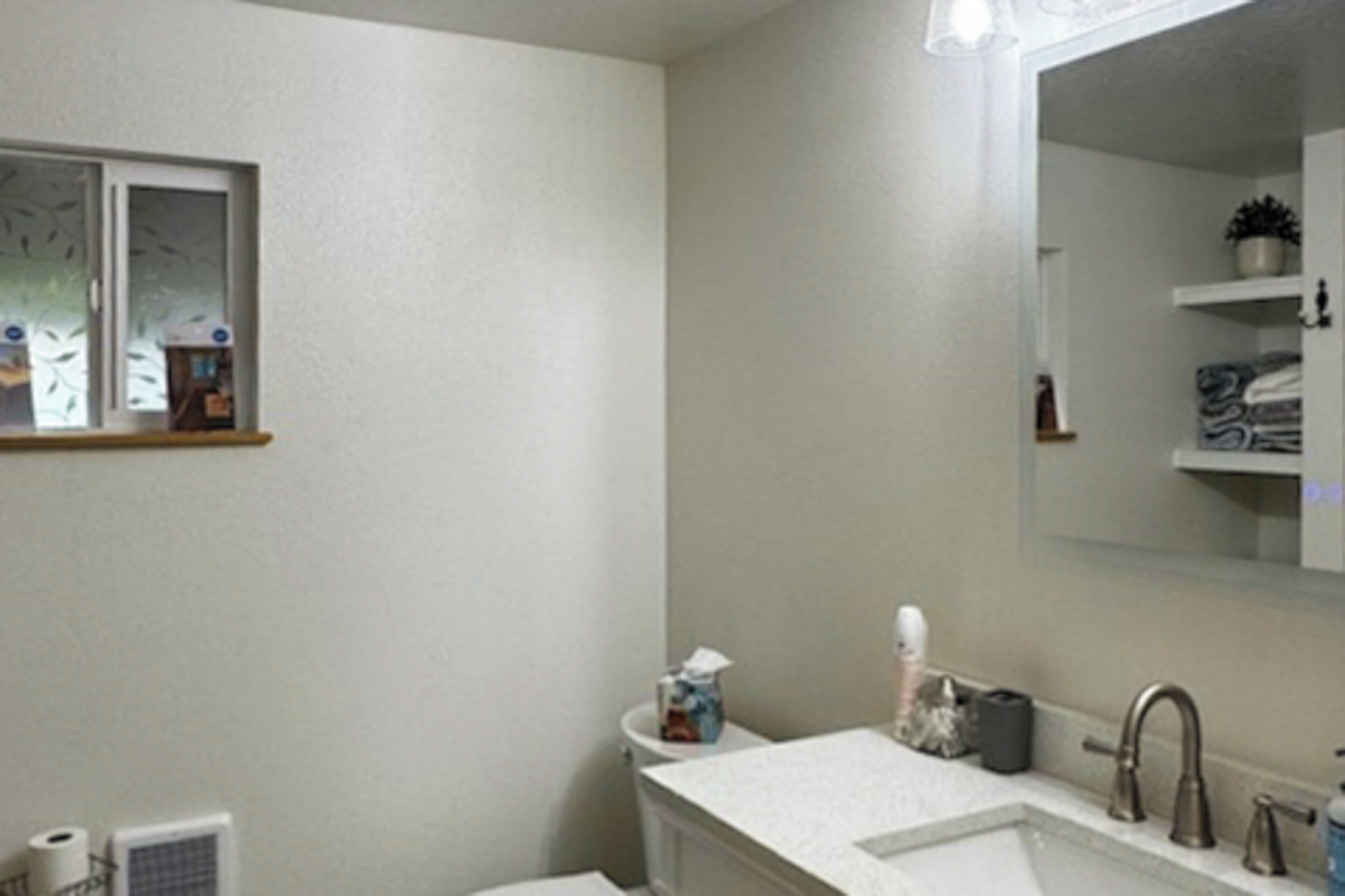 A bathroom with a white sink, a mirror, a window with frosted glass, and a towel rack.