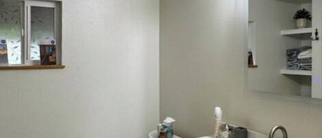A bathroom with a white sink, a mirror, a window with frosted glass, and a towel rack.
