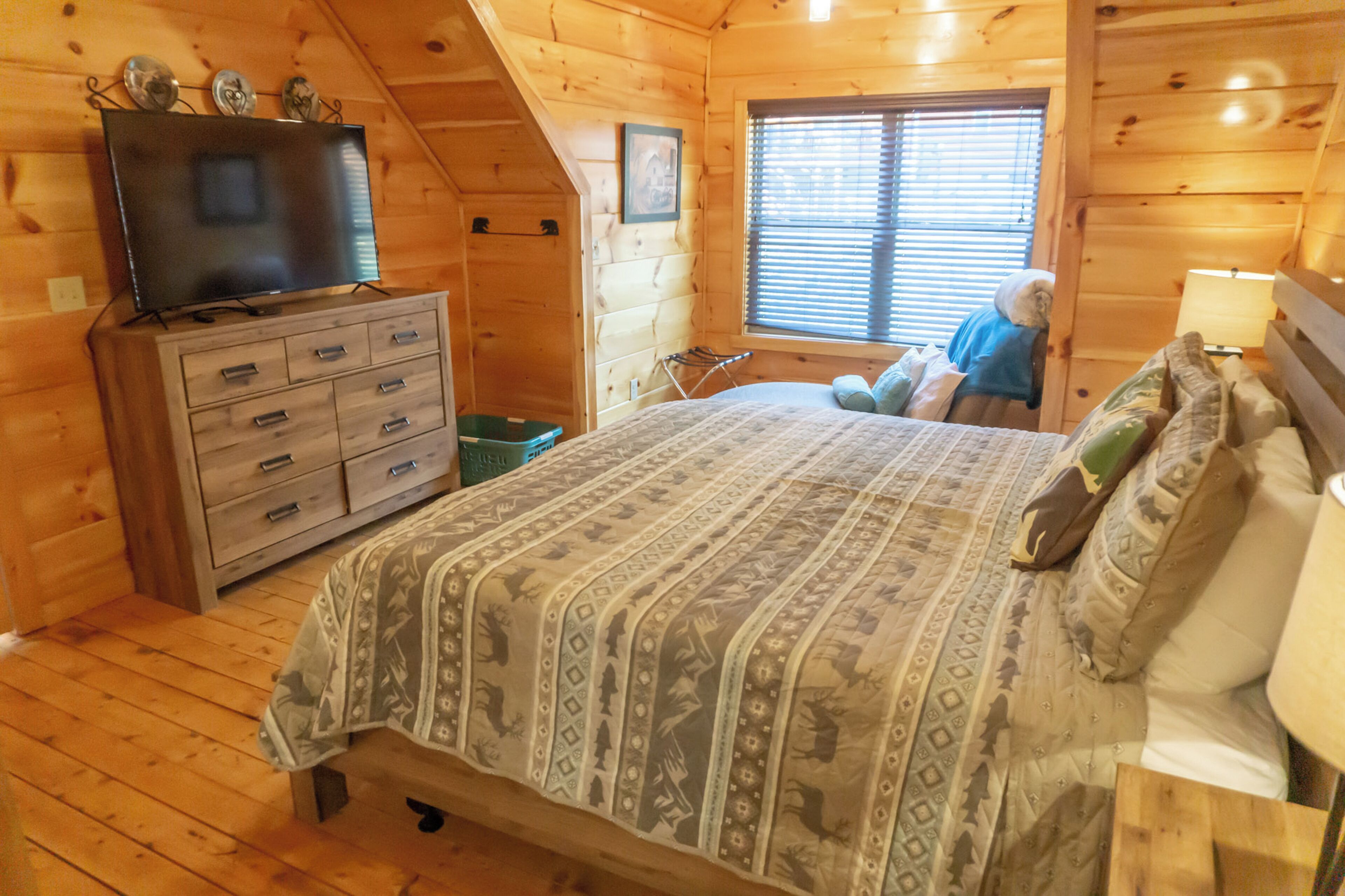 A wooden cabin bedroom with a bed, dresser, and a television on a dresser.