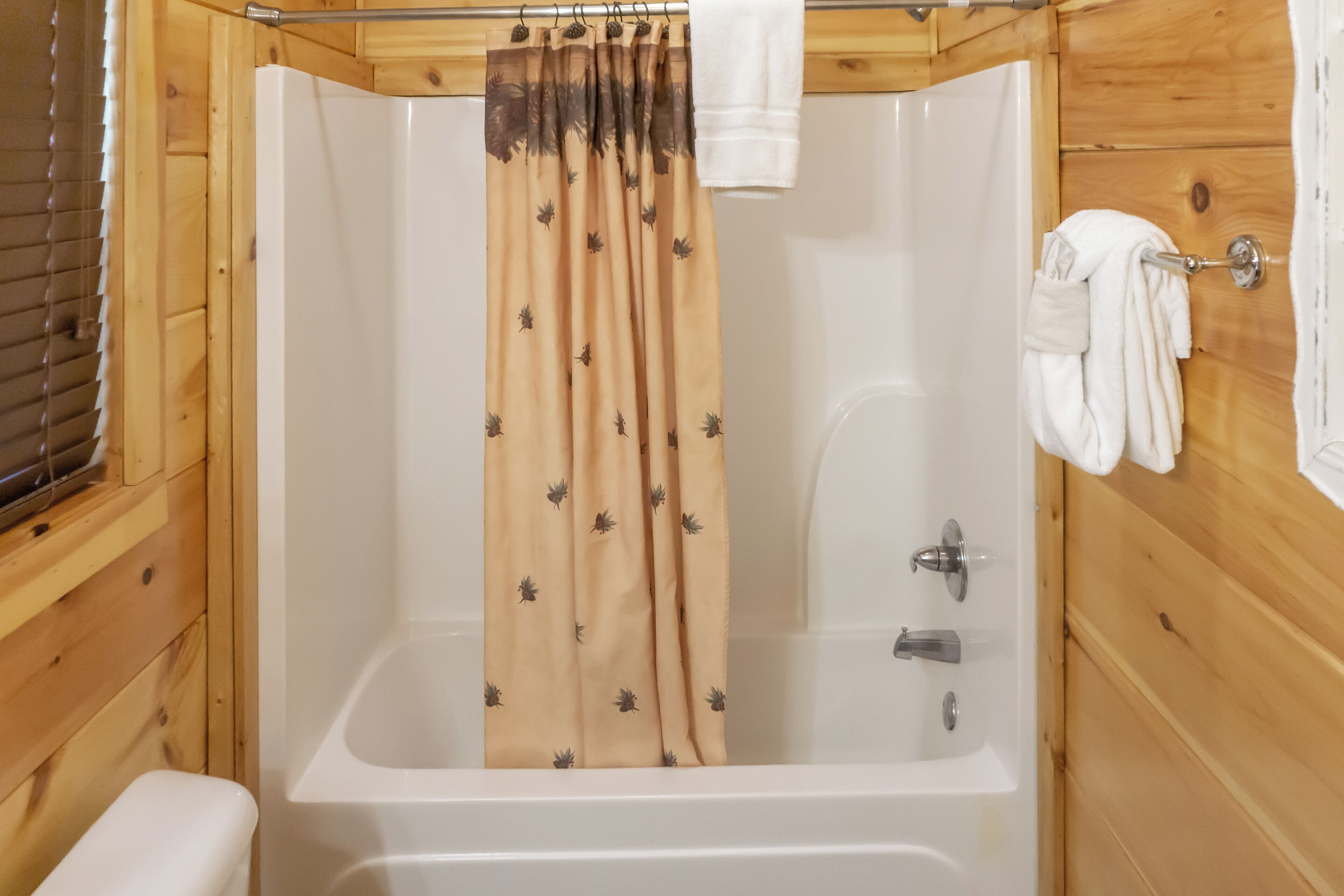 A wooden cabin bathroom with a bathtub, a shower curtain, and a towel rack.