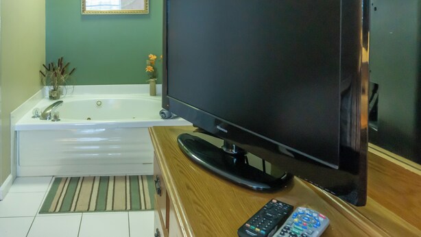 Un baño con una bañera, un televisor sobre un soporte de madera y un control remoto en el soporte.