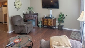 Una sala de estar con un sofá, un sillón y una mesa de centro de vidrio con un reloj.