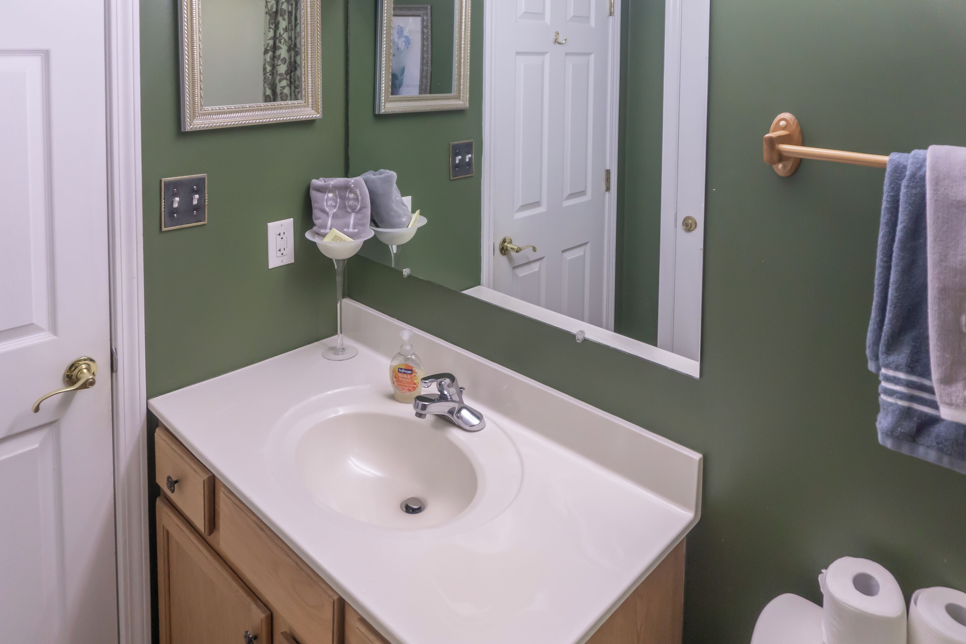 A bathroom with a white sink, green walls, a mirror, and a towel rack.