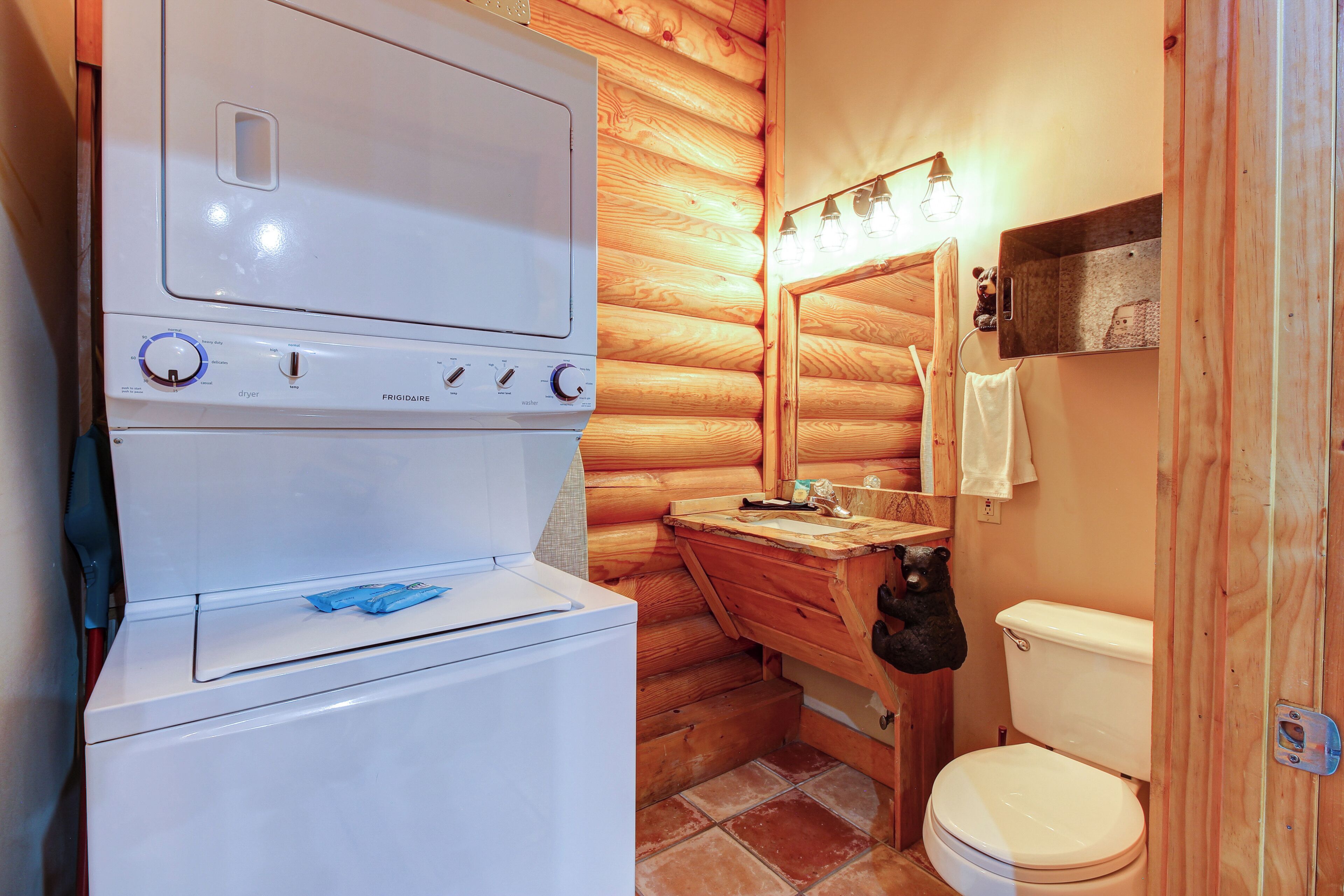 Une petite salle de bain équipée d’un lave-linge, d’un meuble-lavabo en bois, de toilettes et d’un miroir avec éclairage.