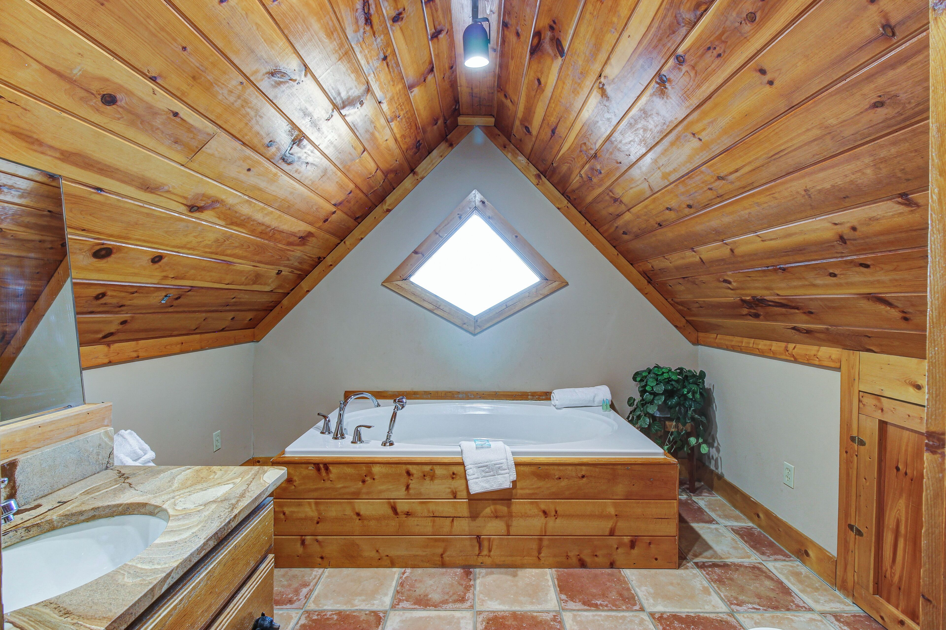 Un baño de cabaña de madera con tragaluz, una bañera y un lavabo.