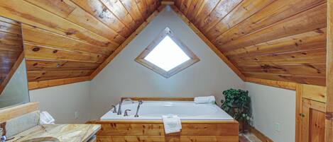 Un baño de cabaña de madera con tragaluz, una bañera y un lavabo.