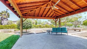 A covered patio area with a wooden ceiling and a ceiling fan, featuring a green sofa and a small table. - Two Dog-friendly Home, Close to Wine Country (Fallbrook)