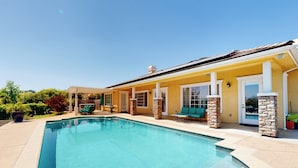 A pool area with a yellow building, stone pillars, and a covered seating area. - Two Dog-friendly Home, Close to Wine Country (Fallbrook)