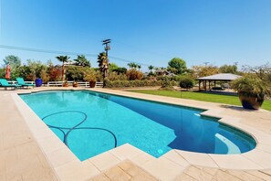 Ein rechteckiger Swimmingpool mit gefliestem Sonnendeck, umgeben von Liegestühlen und Pflanzen in Töpfen.