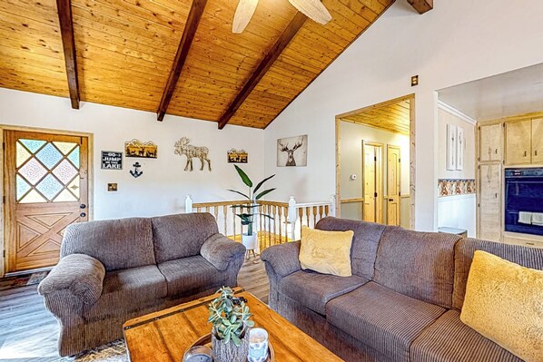 A spacious living room with two sofas, a wooden coffee table, and a staircase leading to another room. - Idyllic Cabin in the Woods: Cozy Crestline Retreat (Crestline)