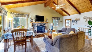 A cozy living room with a fireplace, wooden ceiling beams, and a television. - Idyllic Cabin in the Woods: Cozy Crestline Retreat (Crestline)
