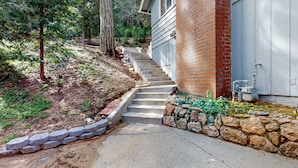 A residential property with a stone retaining wall, a concrete staircase leading to a garage, and a brick exterior wall. - Idyllic Cabin in the Woods: Cozy Crestline Retreat (Crestline)
