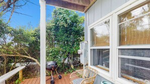 A wooden deck with a wicker chair and a small table, a barbecue grill, and a window with blinds. - Entire House - Serenity in Surf City (Holly Ridge)