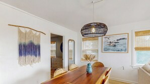 A dining area with a wooden table, woven chairs, a blue vase, and a hanging light fixture. - Entire House - Serenity in Surf City (Holly Ridge)