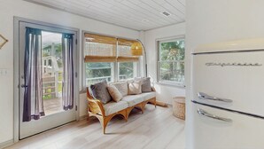 A modern kitchen with a white refrigerator, a wooden bench with cushions, and a view of a wooden deck through the glass door. - Entire House - Serenity in Surf City (Holly Ridge)