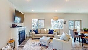 A modern living room with a fireplace, a sofa, a coffee table, and a dining area with a table and chairs. - Crooked River 10 A - Entire Home! (Brian Head)