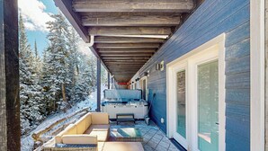 A covered outdoor area with a hot tub, seating, and a view of snow-covered trees. - Crooked River 10 A - Entire Home! (Brian Head)