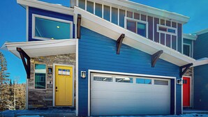 A two-story house with a stone foundation, a yellow front door, and a white garage door. - Crooked River 10 A - Entire Home! (Brian Head)
