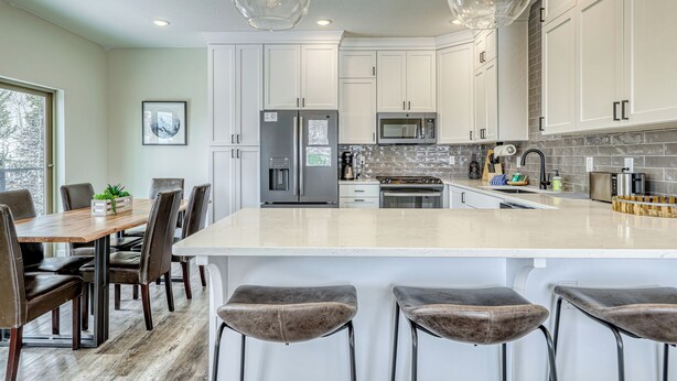 A modern kitchen with white cabinets, a large island with bar stools, stainless steel appliances, and pendant lighting. - Crooked River 10 A - Entire Home! (Brian Head)