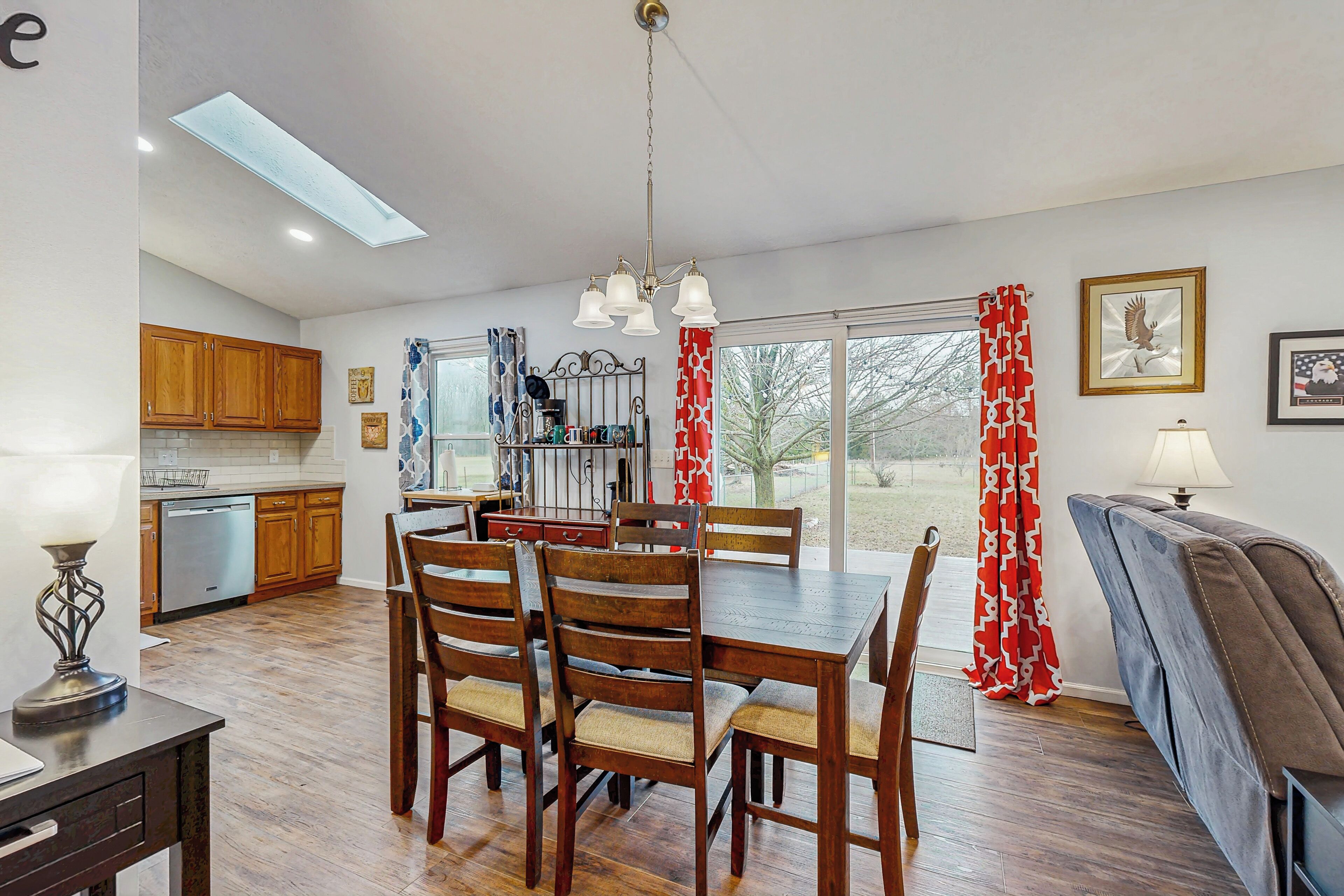 A dining area with a wooden table and chairs, a kitchen with wooden cabinets, and a view through a glass door.