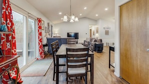 A dining area with a wooden table and chairs, a chandelier, and a television in the background.