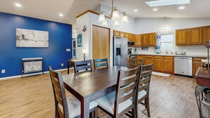 A modern kitchen with wooden cabinets, a dining table with chairs, a refrigerator, and a dishwasher.