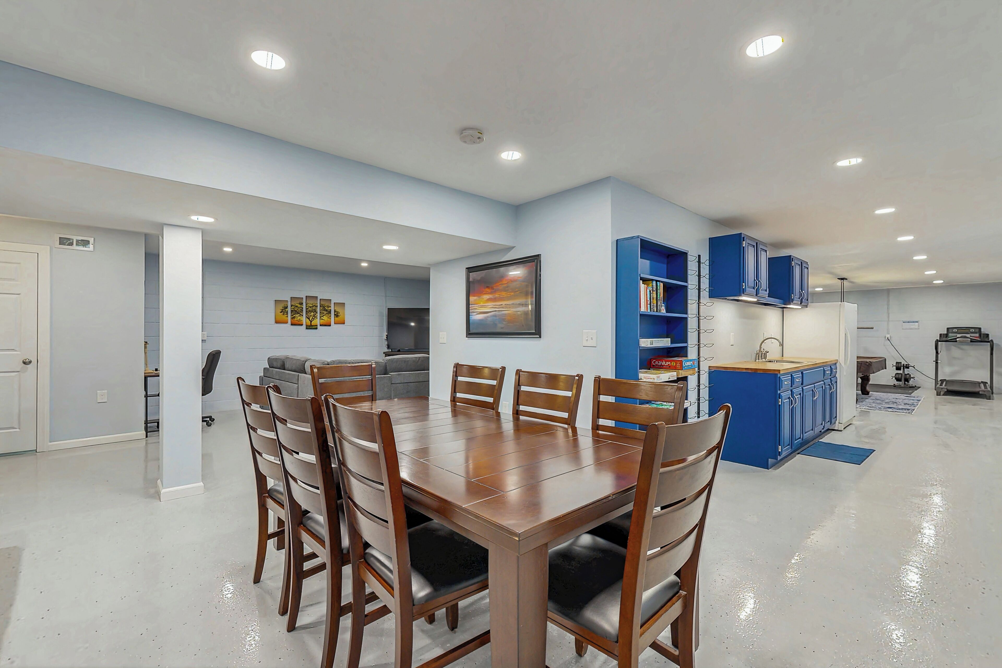 Une cuisine moderne avec des meubles bleus, un coin repas avec une table et des chaises en bois, et un tableau accroché au mur.