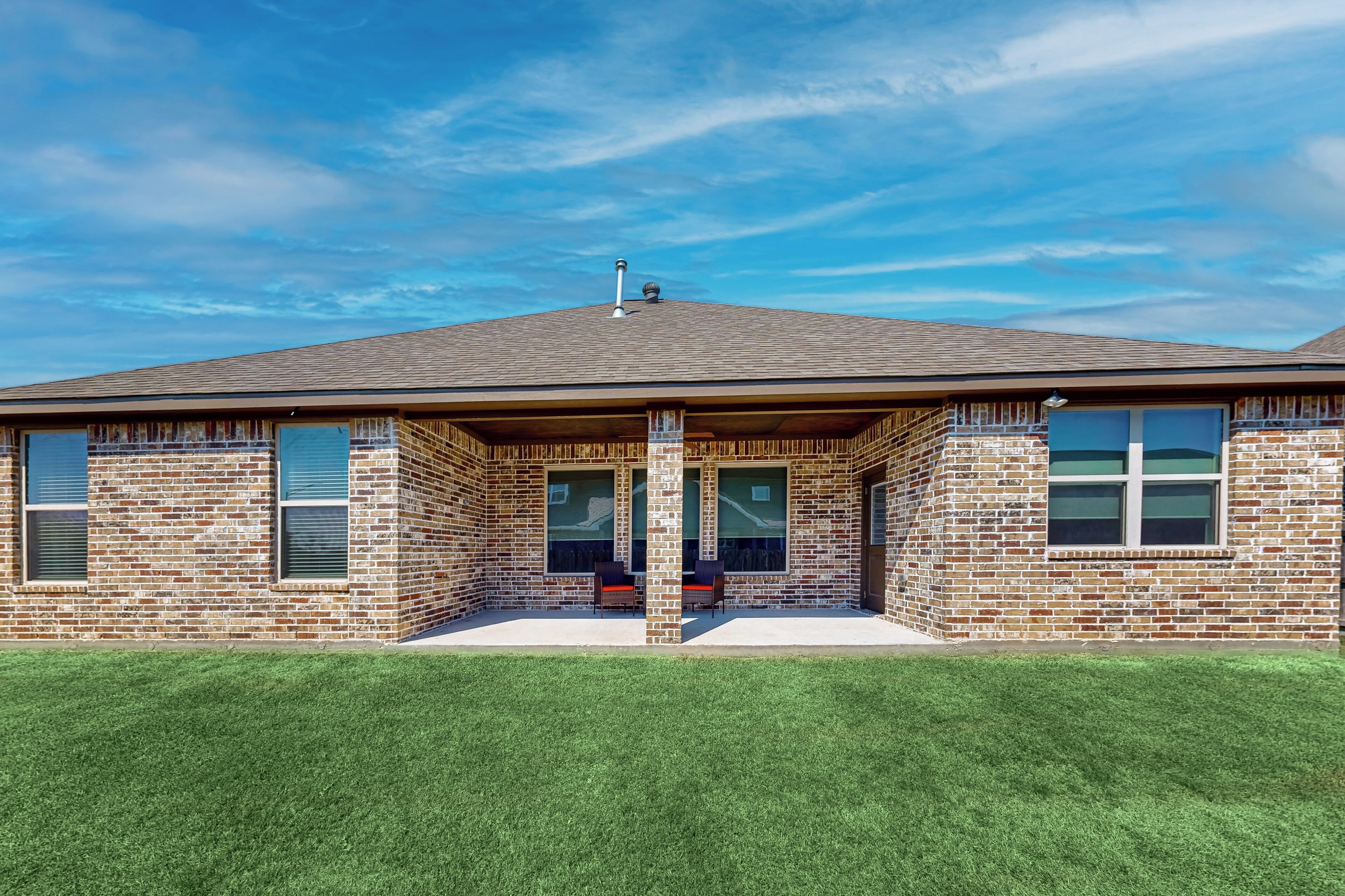 A two-story brick building with a flat roof, large windows, and a covered patio area.