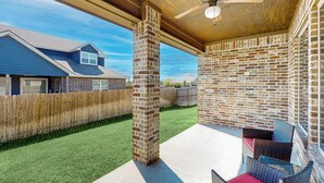 Un patio couvert avec des murs en briques, un ventilateur de plafond et des sièges d’extérieur.