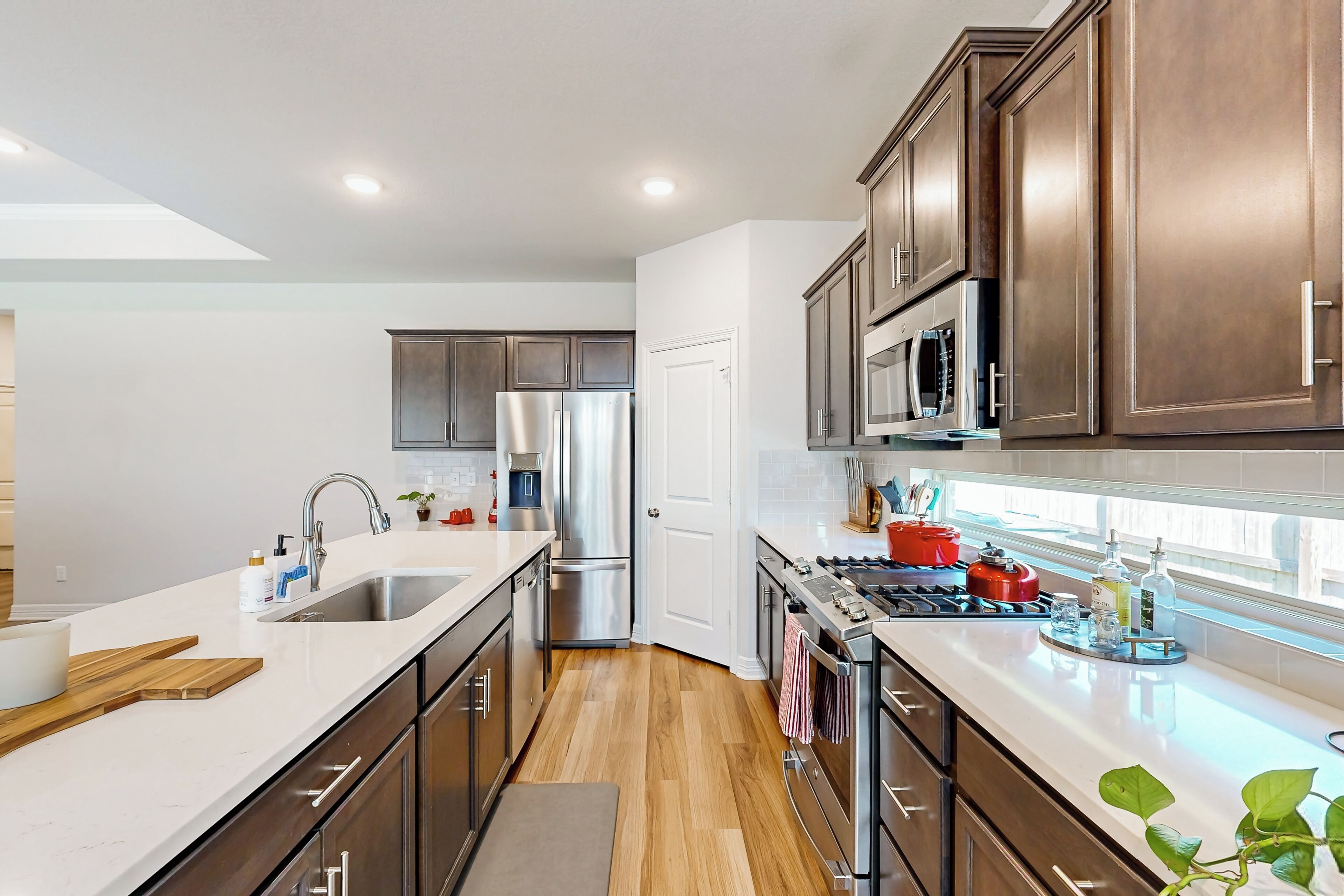 A modern kitchen with stainless steel appliances, wooden cabinets, and a large window providing natural light.