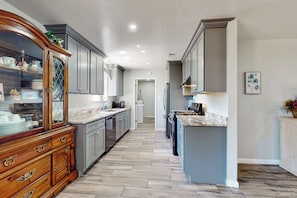 A kitchen with grey cabinets, a wooden cabinet with glass doors, a marble countertop, and a tiled floor. - 3BR Family-friendly Home w/ Patio & BBQ (Fredericksburg)