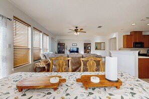 Un salon spacieux avec un grand canapé, une table à manger accompagnée de deux petites tables d’appoint en bois, et un coin cuisine doté de meubles en bois et d’un four à micro-ondes.