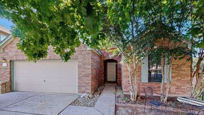 A residential garage with a brick exterior, a driveway leading to a front door, and a small patio area with outdoor furniture. - Inviting Home w/ Enlosed Yard & Gas Grill (Round Rock)
