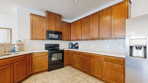A kitchen with wooden cabinets, a black microwave, a stainless steel refrigerator, and a tiled floor. - Inviting Home w/ Enlosed Yard & Gas Grill (Round Rock)